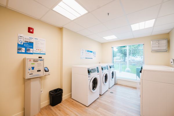 Shared laundry room featuring a utility sink, three washing machines, three dryers, and a laundry card reloading machine for convenient on-site laundry and easy card balance top-ups.