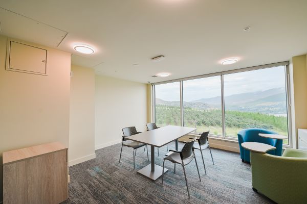 Study room featuring a table with four chairs, a single-person couch, and a swivel desk chair, with a large window providing natural light for a comfortable space to study, work, or relax.