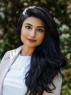 a woman wearing a white t shirt and a light purple blazer with long black hair looks at the camera smiling