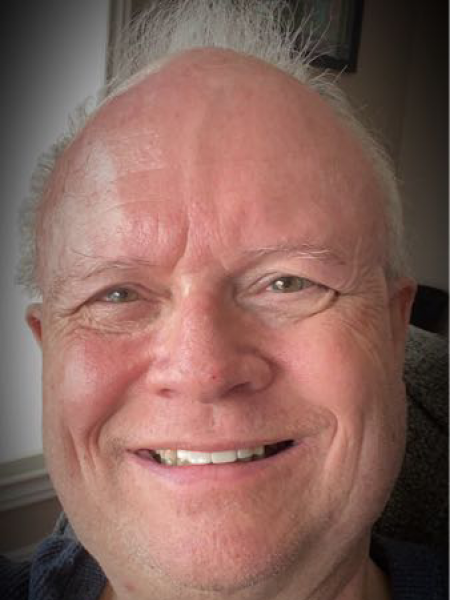 A man with white hair smiles at the camera