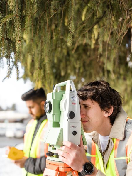 Civil Engineering program student looking into surveying equipment while another student manually records data set