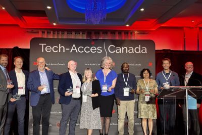 Tech-Access Canada award recipients stand together holding their trophies and smiling.
