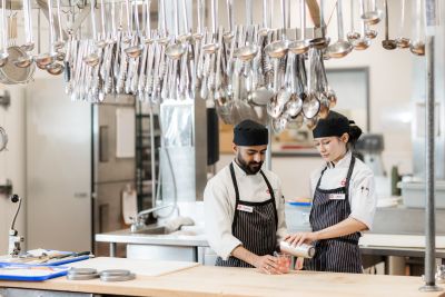 two culinary students stand in a kitchen pouring a drink