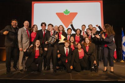 Enactus Okanagan Team celebrating on stage after winning the Enactus National Championship, holding trophies and cheering together.