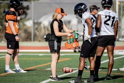 Cassidy Findlay in black shorts and orange ball cap, supports BC Lions players at training camp