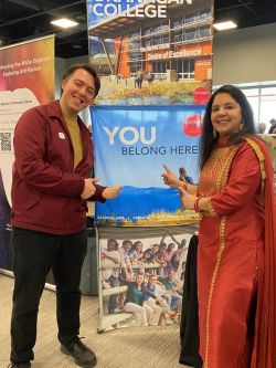 Two people point to an OC sign that says "You belong here"