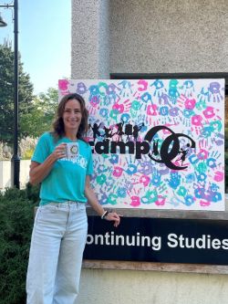 Amanda standing in front of Camp OC sign, wearing a green shirt and blue jeans.