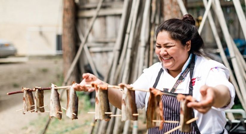 Culinary Arts student shows off salmon fillets on stakes that will go onto the fire.