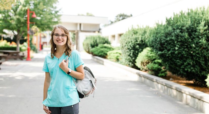 Student Mariah Perry stands in the Kelowna campus courtyard clutching her backpack in nursing scrubs