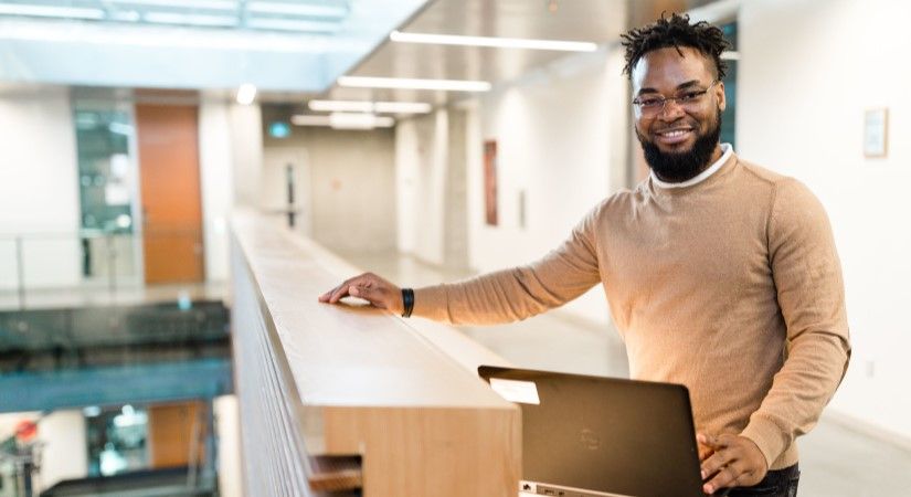 Student rests hand and laptop against ledge of counter in the atrium of the trades building