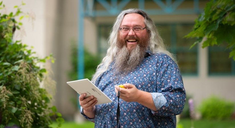 Student smiles at the camera while holding papers and a stop watch
