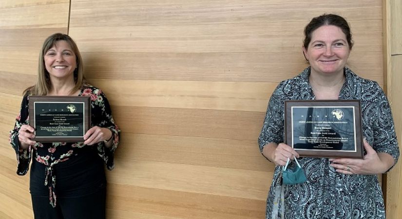 Kerry Rempel and Kyleen Myrah hold up conference plaques in the Centre for Learning