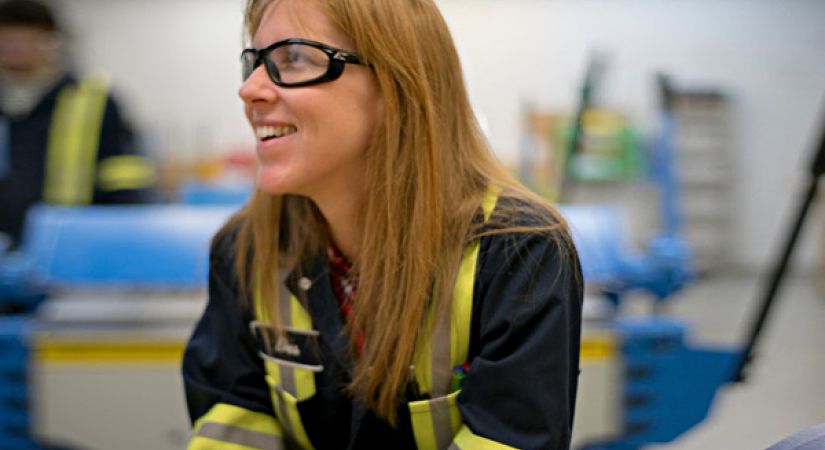 A female trades student with medium length blonde hair looks off to the side. 