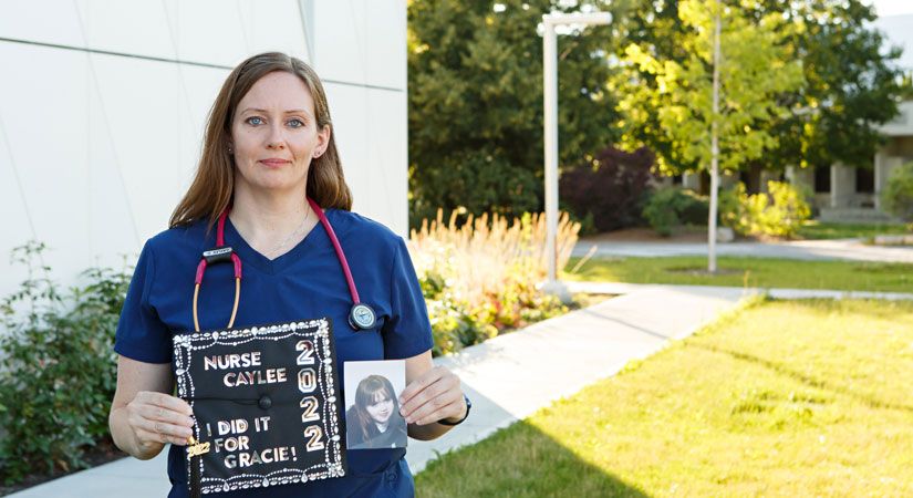 Caylee wearing her nursing scrubs holding a graduation cap and a photo of her late child