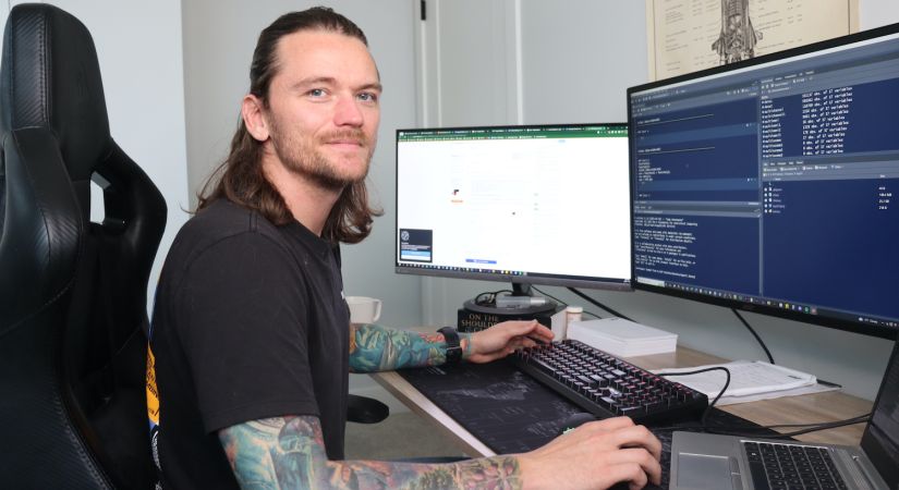 ELEN graduate works remotely from home, sitting at his computer desk with multiple screens.