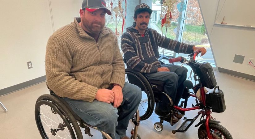 Two men in wheeled mobility aids in a classroom