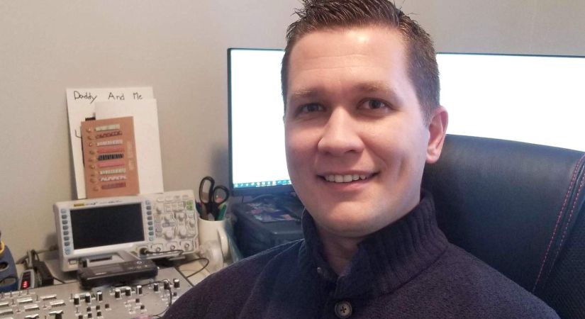 ELEN alumnus Aaron Edis sits in front of a computer and electronics components.