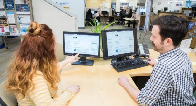 two people sitting at a desk looking at a computer screen
