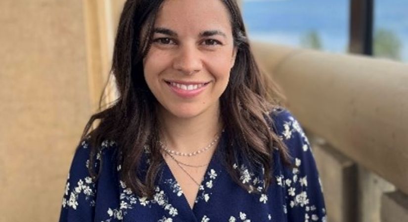 woman with brown hair, wearing a blue long sleeve shirt and standing on a balcony