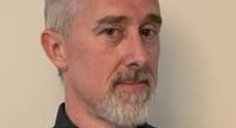 Steven Crema stands smiling infront of a while background