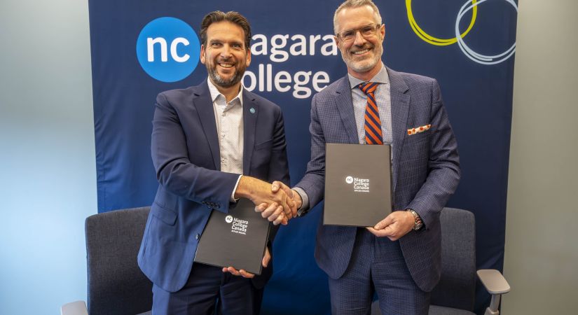 two men shaking hands and holding copies of the agreement