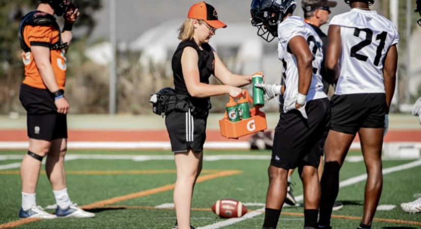 Cassidy Findlay in black shorts and orange ball cap, supports BC Lions players at training camp
